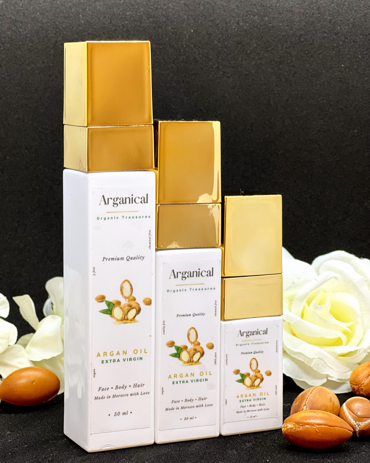 Arganical trio argan oil 50ml 30ml and 15ml bottles with gold cap on a dark background with argan nuts.